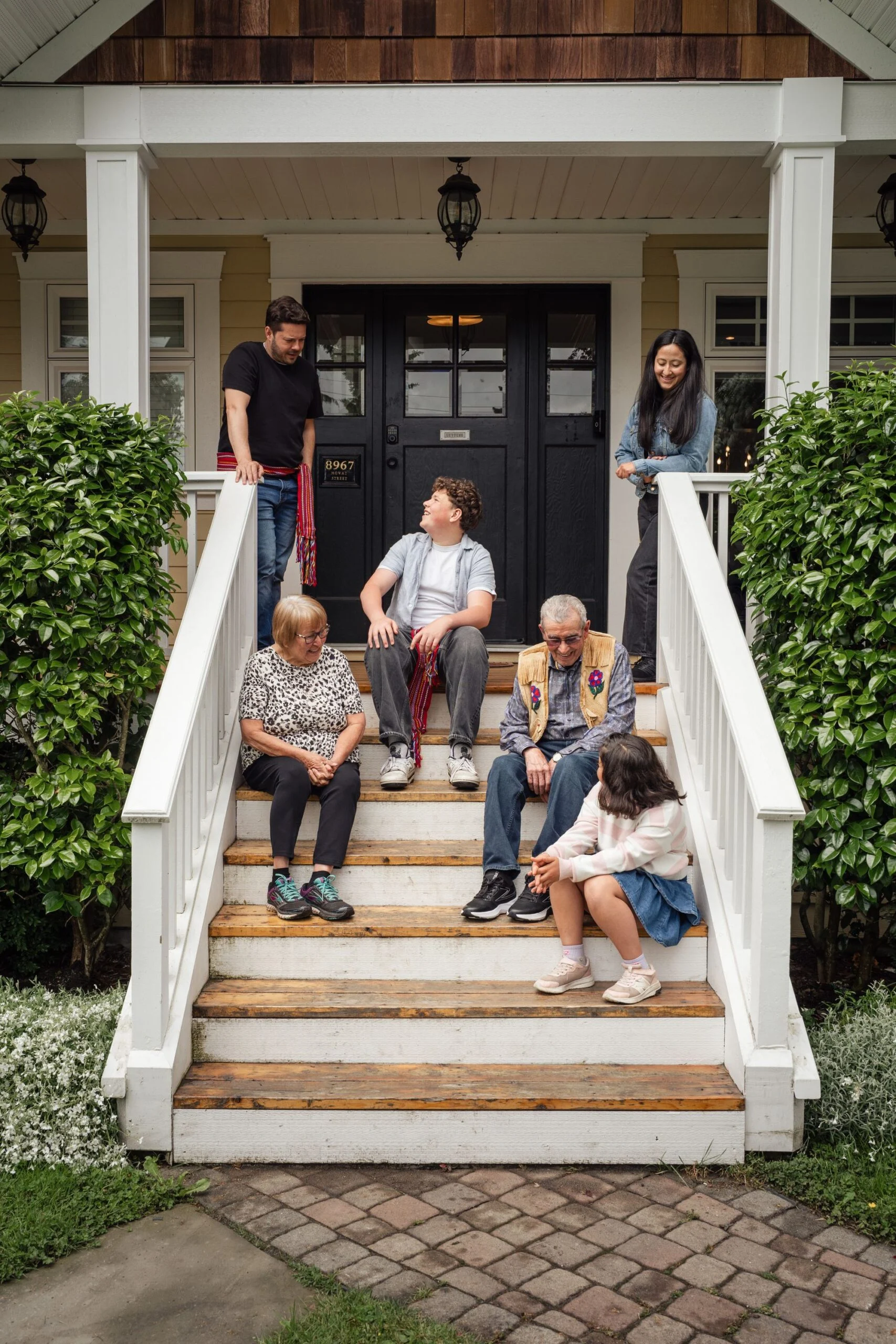 A family sitting together on the porch steps of a white house